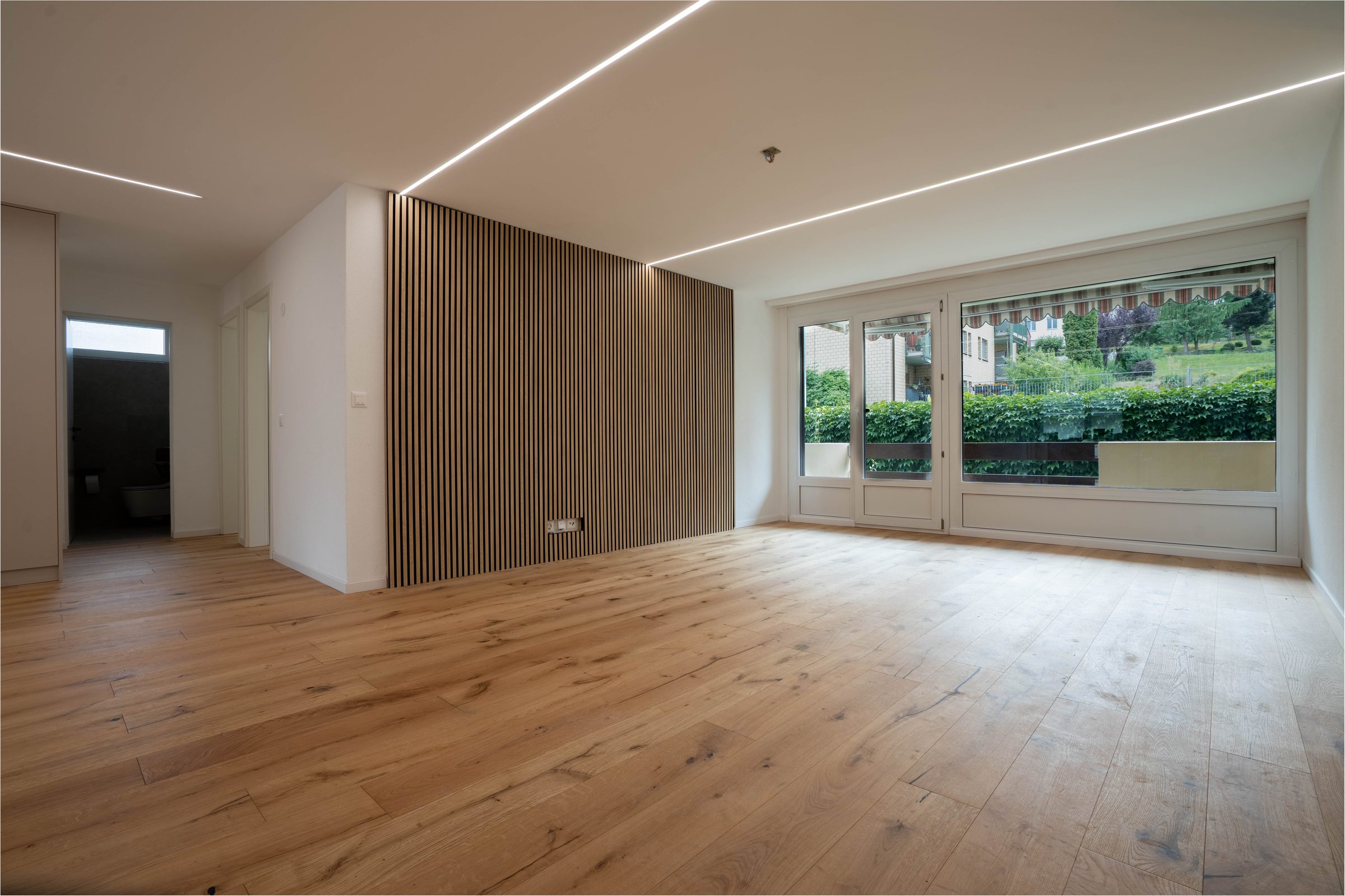 Wohnzimmer mit Holzlamellenwand und Blick ins Grüne